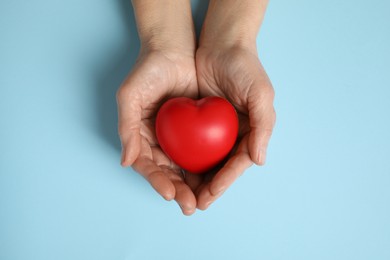 Photo of Elderly woman holding red heart in hands on light blue background, top view