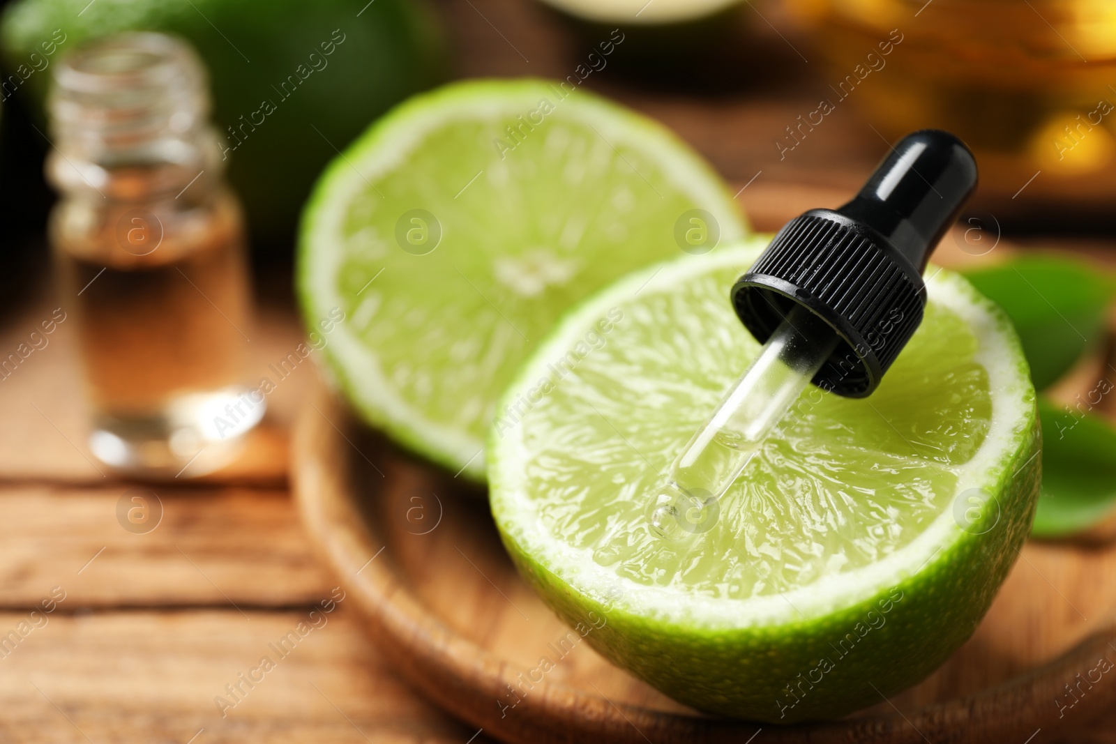 Photo of Dropper with lime essential oil and cut citrus fruit on wooden table, closeup