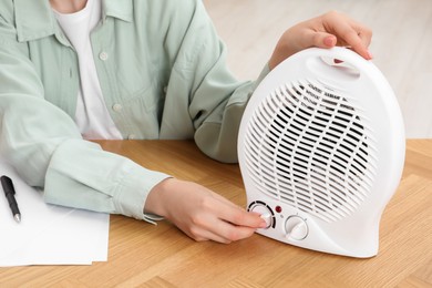 Photo of Young woman adjusting temperature on modern electric fan heater at wooden table, closeup