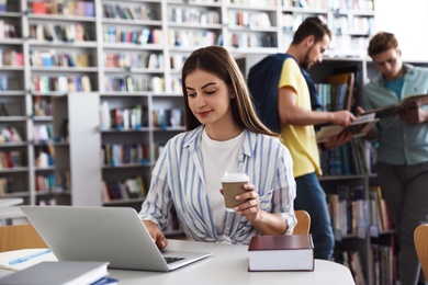 Photo of Young woman studying at table in modern library