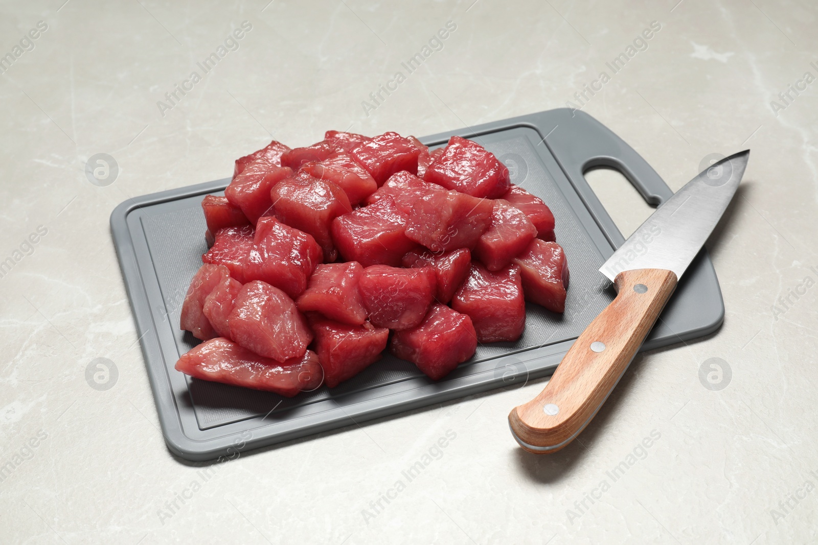 Photo of Cooking delicious goulash. Raw beef meat and knife on light grey table