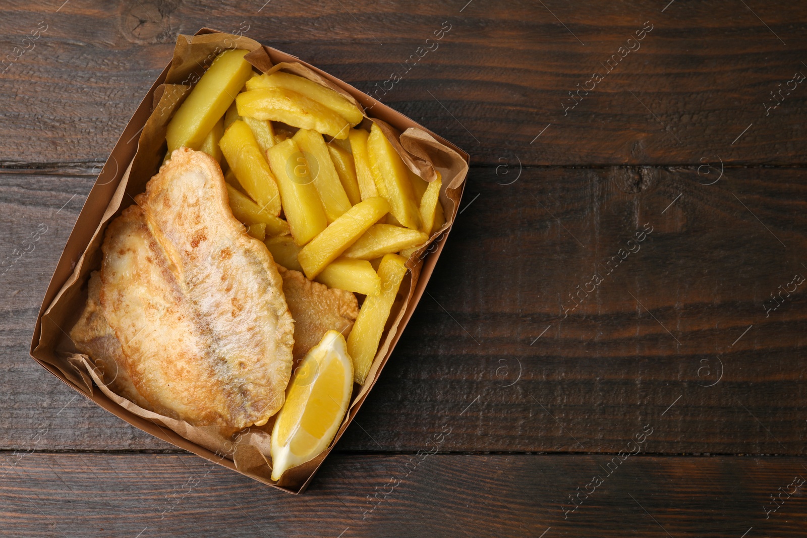 Photo of Delicious fish and chips in paper box on wooden table, top view. Space for text