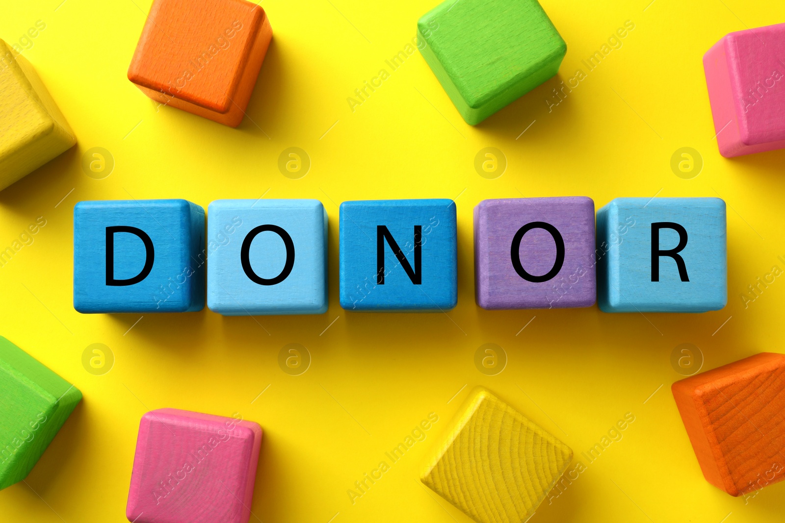 Photo of Word Donor made of colorful wooden cubes on yellow background, flat lay