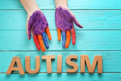 Photo of Woman with painted hands and word "Autism" on wooden background