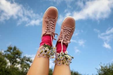 Photo of Woman with beautiful tender flowers in socks against blue sky, closeup