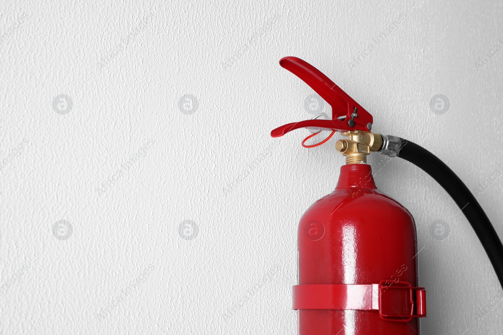 Photo of Fire extinguisher hanging on white wall, closeup. Space for text