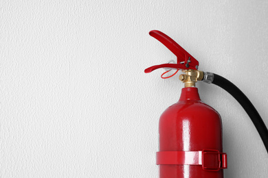 Photo of Fire extinguisher hanging on white wall, closeup. Space for text