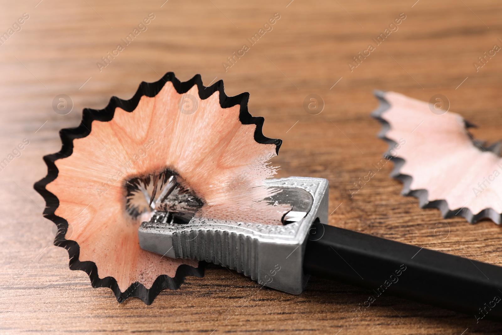 Photo of Metal sharpener with pencil shavings on wooden table, closeup