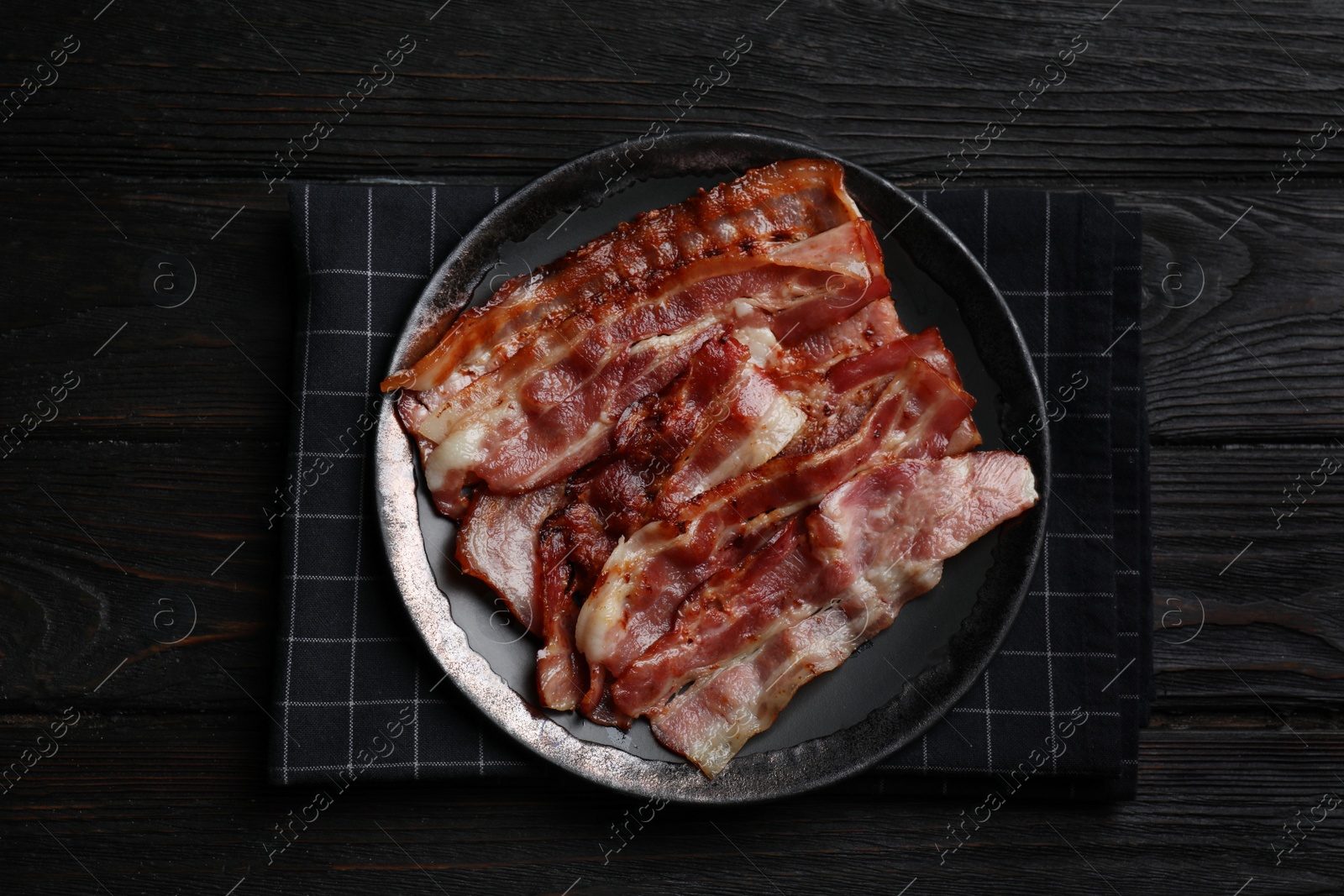 Photo of Slices of tasty fried bacon on black wooden table, top view