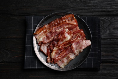 Slices of tasty fried bacon on black wooden table, top view