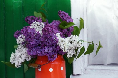 Photo of Beautiful lilac flowers in milk can near house outdoors