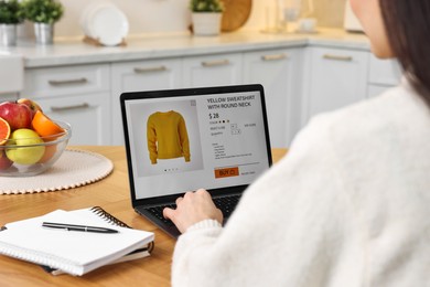 Photo of Woman with laptop shopping online at wooden table in kitchen, closeup