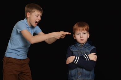 Boy laughing and pointing at upset kid on black background. Children's bullying