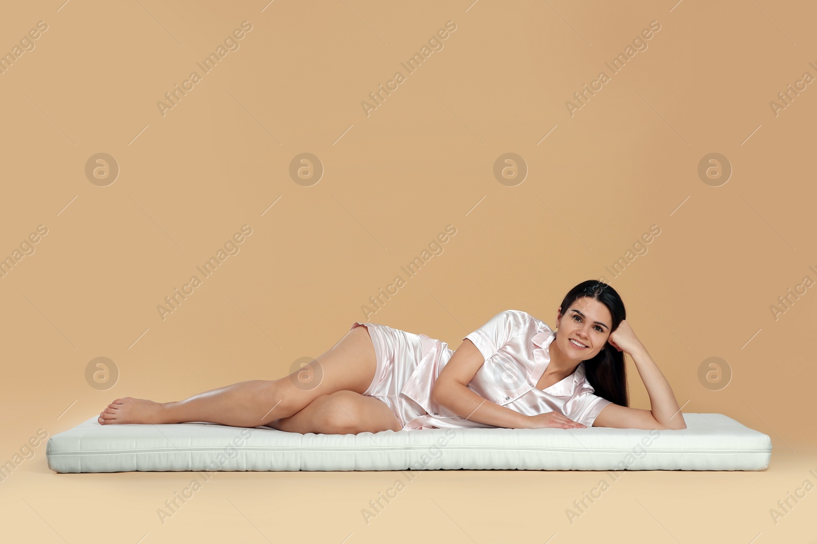 Photo of Young woman lying on soft mattress against beige background