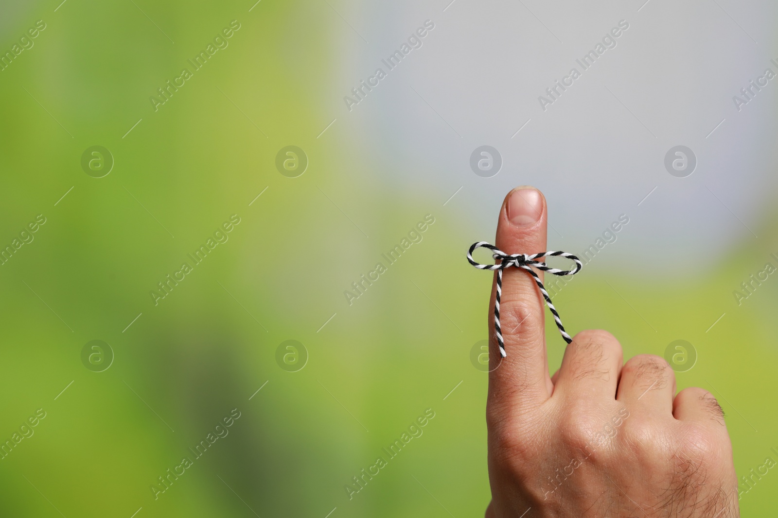 Photo of Man showing index finger with tied bow as reminder on green blurred background, closeup. Space for text