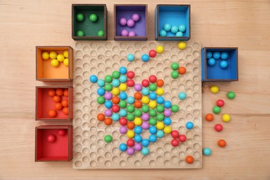 Photo of Wooden sorting board and boxes with colorful balls on table, flat lay. Montessori toy