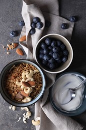 Photo of Tasty granola in bowl, blueberries, yogurt and spoon on gray textured table, flat lay