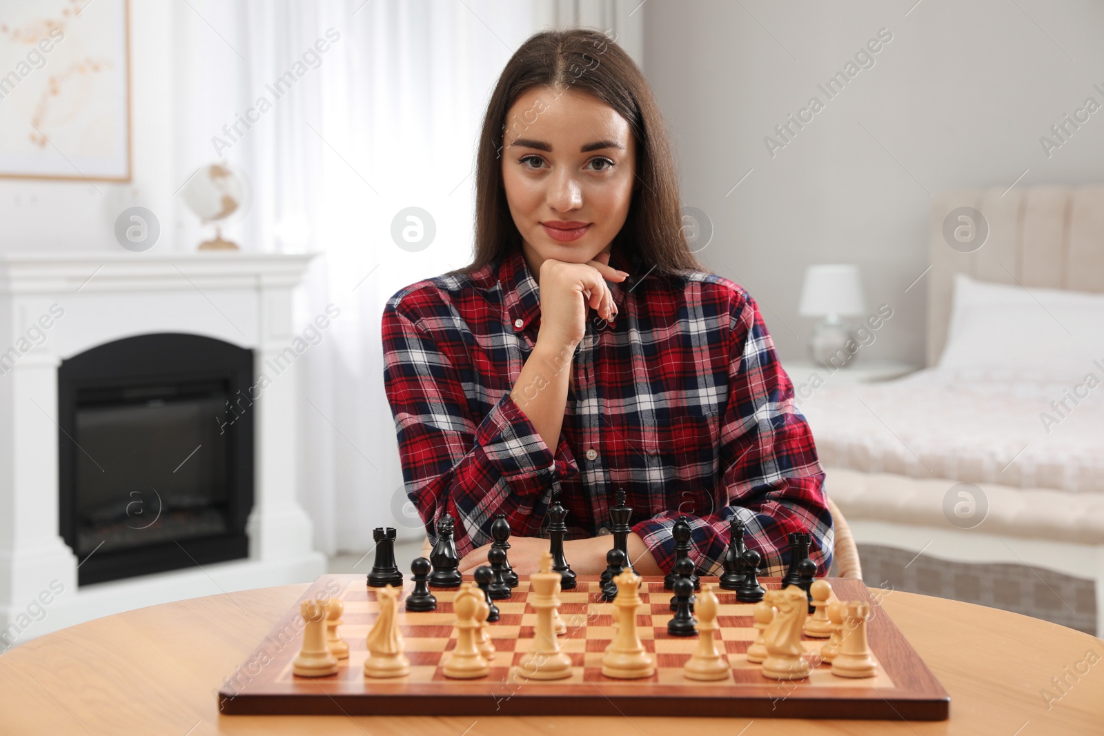 Photo of Young woman playing chess at table in bedroom