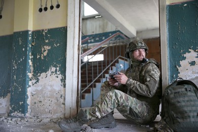 Photo of Military mission. Soldier in uniform with drone controller inside abandoned building