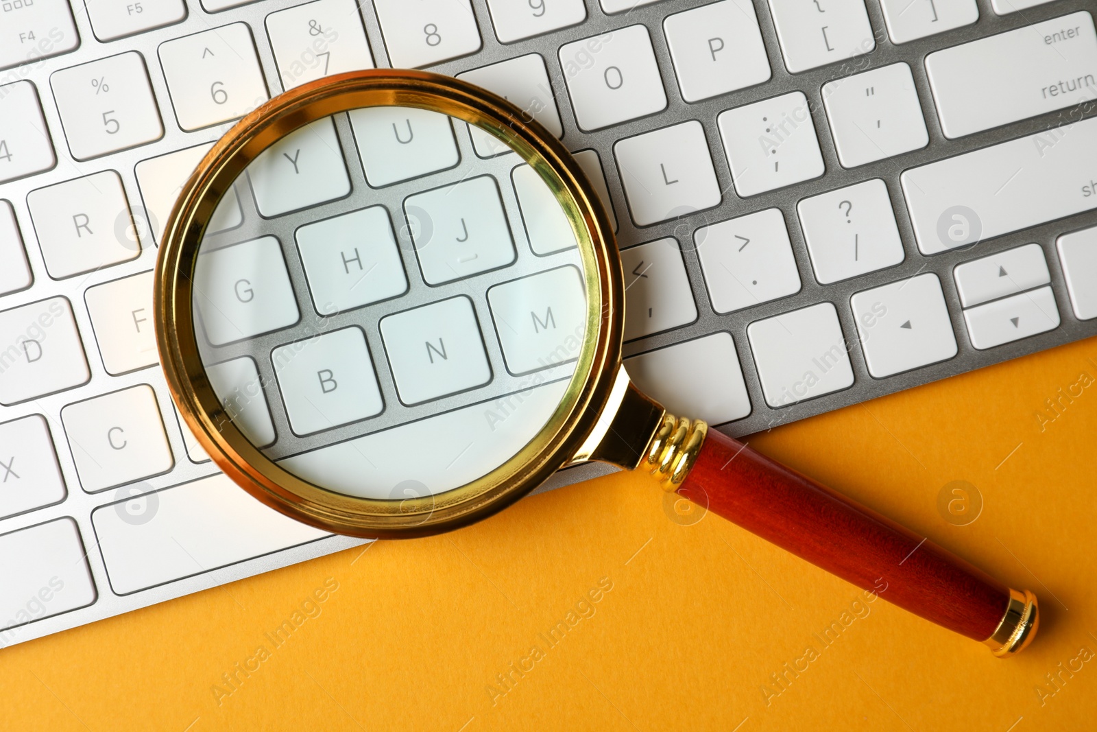 Photo of Magnifier glass and keyboard on orange background, flat lay. Find keywords concept