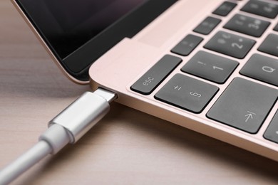 Photo of USB cable plugged into laptop port on light wooden table, closeup
