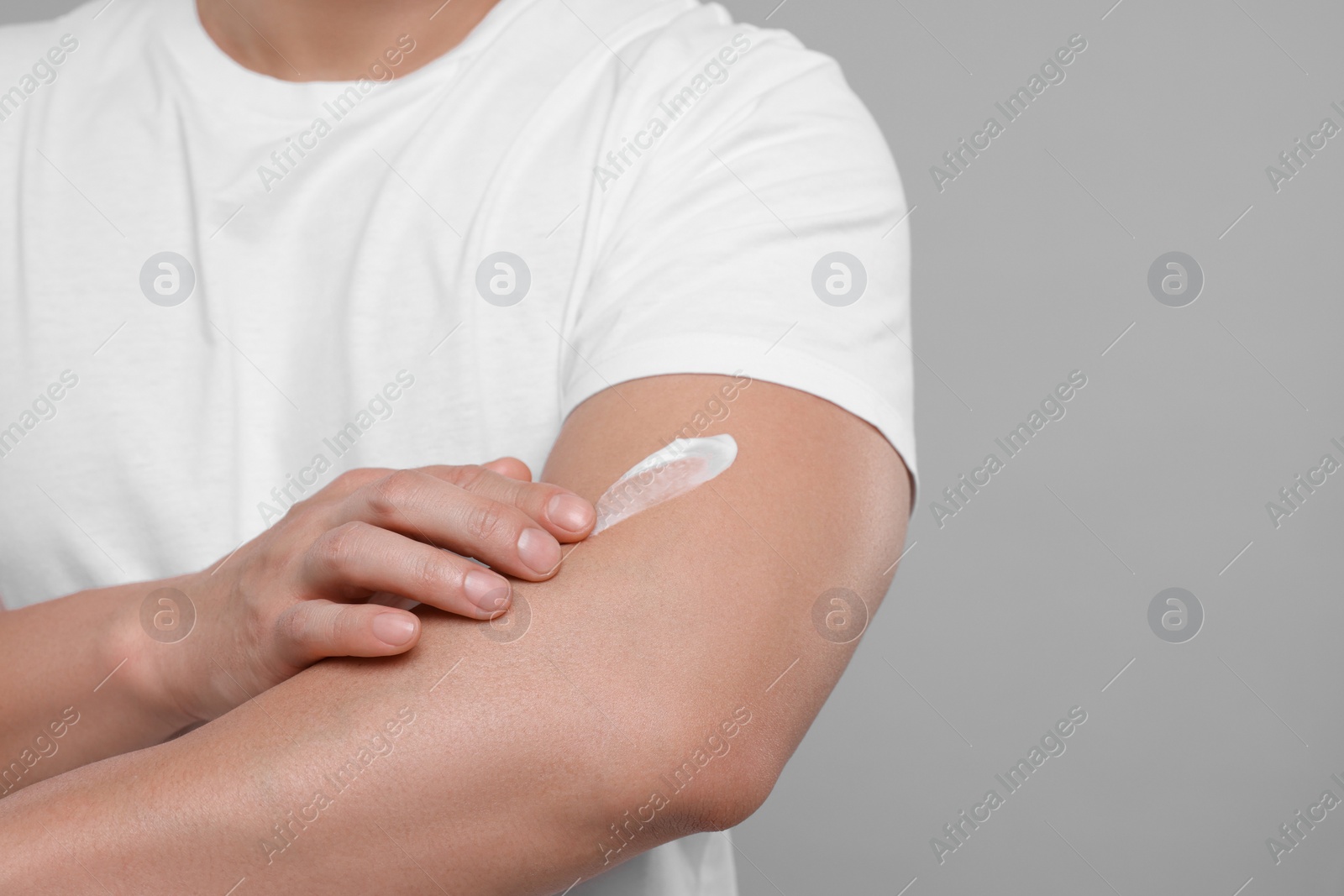 Photo of Man applying body cream onto his arm on light grey background, closeup. Space for text