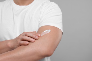 Photo of Man applying body cream onto his arm on light grey background, closeup. Space for text