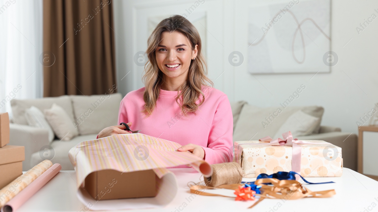 Photo of Beautiful young woman wrapping gift at table in living room