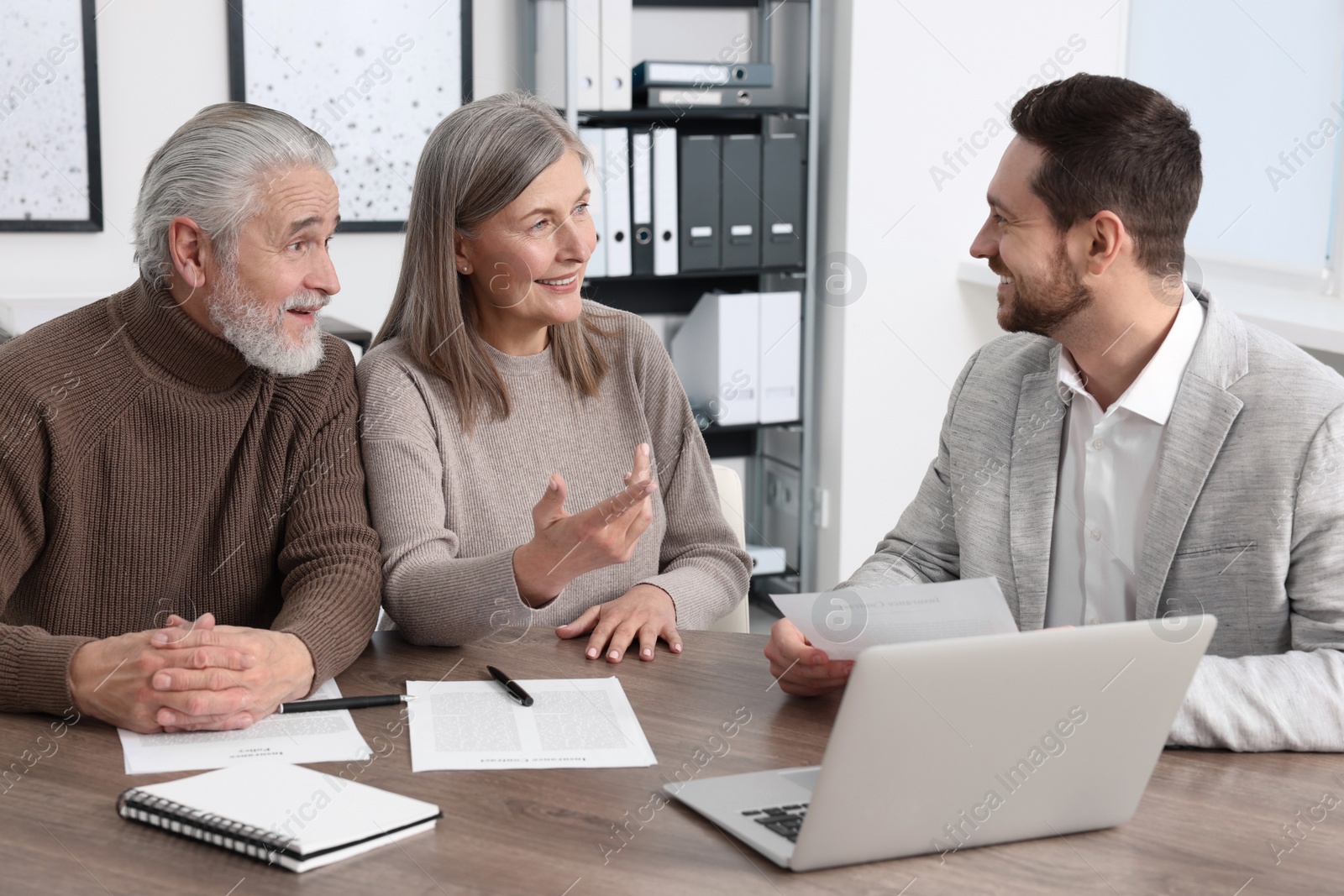 Photo of Elderly couple consulting insurance agent about pension plan at wooden table indoors