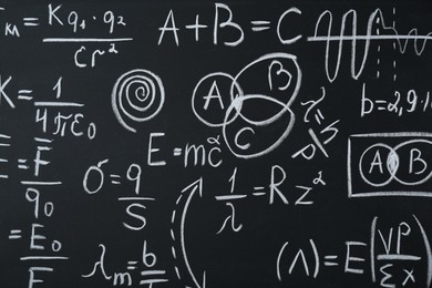 Photo of Different physical formulas written with chalk on blackboard, closeup