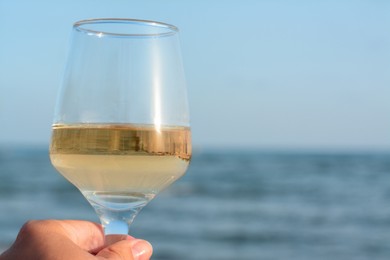 Woman holding glass of tasty wine near sea, closeup. Space for text
