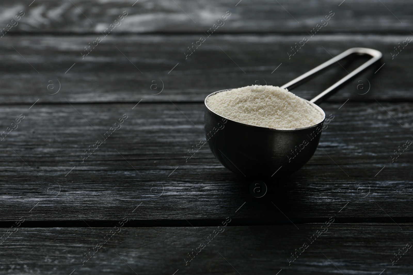 Photo of Measuring scoop of protein powder on dark wooden table. Space for text