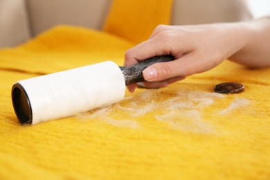 Photo of Woman removing hair from yellow knitted jacket with lint roller, closeup