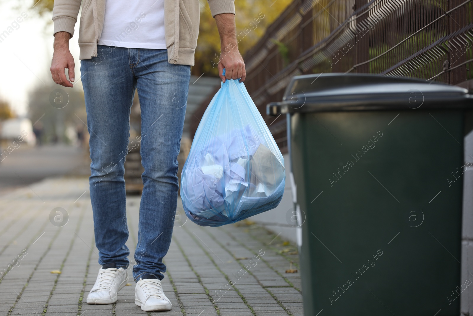 Photo of Man carrying garbage bag to recycling bin outdoors, closeup