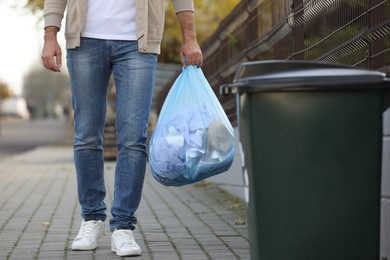 Photo of Man carrying garbage bag to recycling bin outdoors, closeup