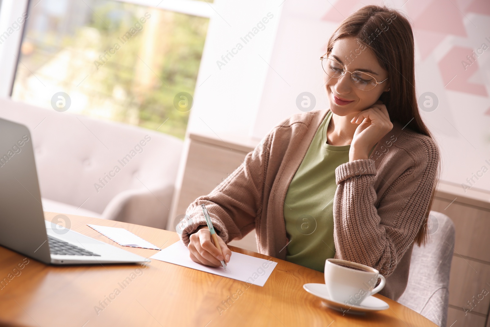 Photo of Woman writing letter at wooden table in room