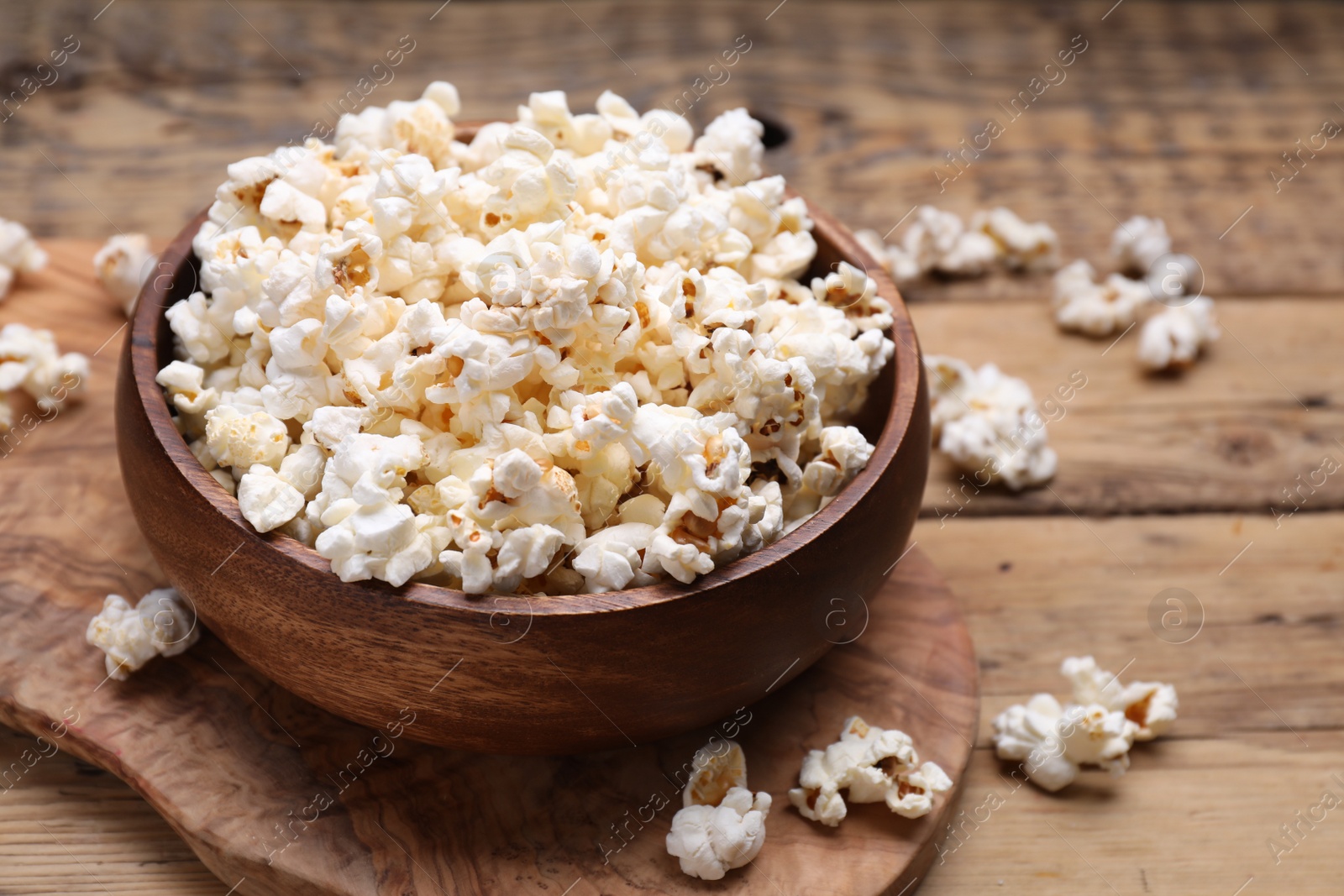 Photo of Bowl of tasty popcorn on wooden table, closeup. Space for text