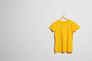 Photo of Hanger with yellow t-shirt on light wall. Mockup for design