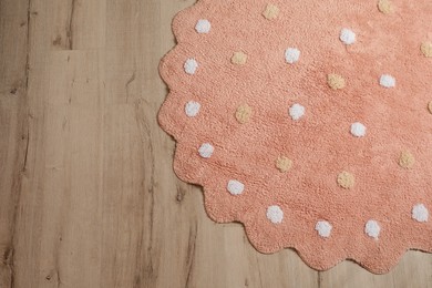 Round pink rug with polka dot pattern on wooden floor, top view. Space for text
