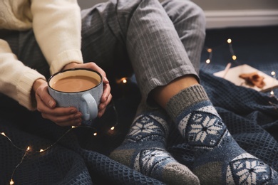 Photo of Woman relaxing with cup of hot winter drink on warm plaid indoors, closeup. Cozy season