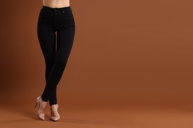 Photo of Woman wearing stylish black jeans and high heels shoes on brown background, closeup. Space for text