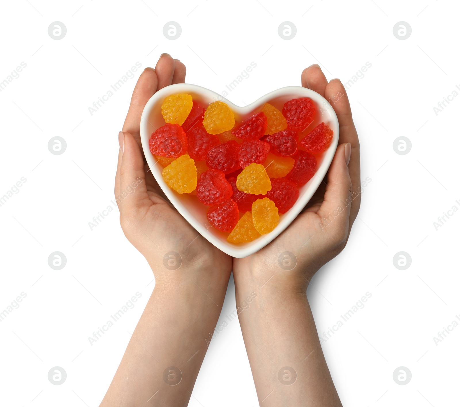 Photo of Woman holding heart shaped bowl with delicious gummy raspberry candies on white background, top view
