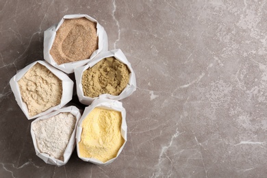 Photo of Bags with different types of flour on grey background, top view. Space for text