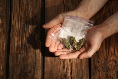 Photo of Man holding plastic bags with cocaine and hemp buds on wooden background, closeup. Space for text