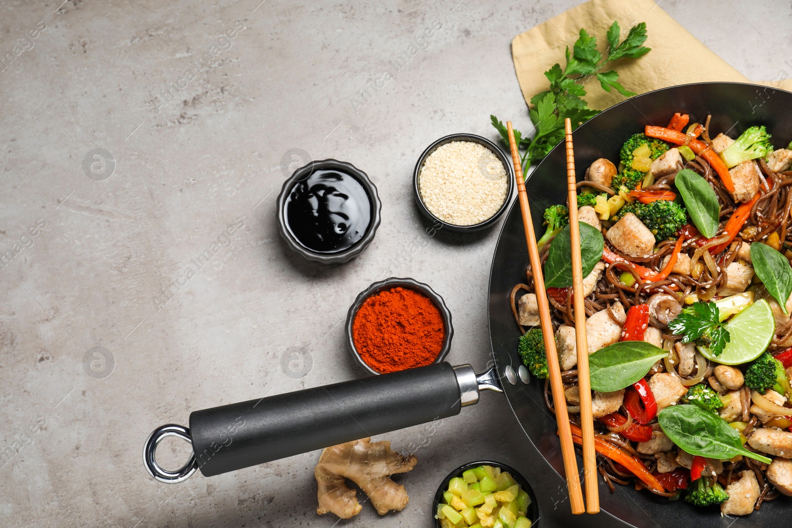 Photo of Stir-fry. Tasty noodles with meat in wok, chopsticks and ingredients on grey textured table, flat lay