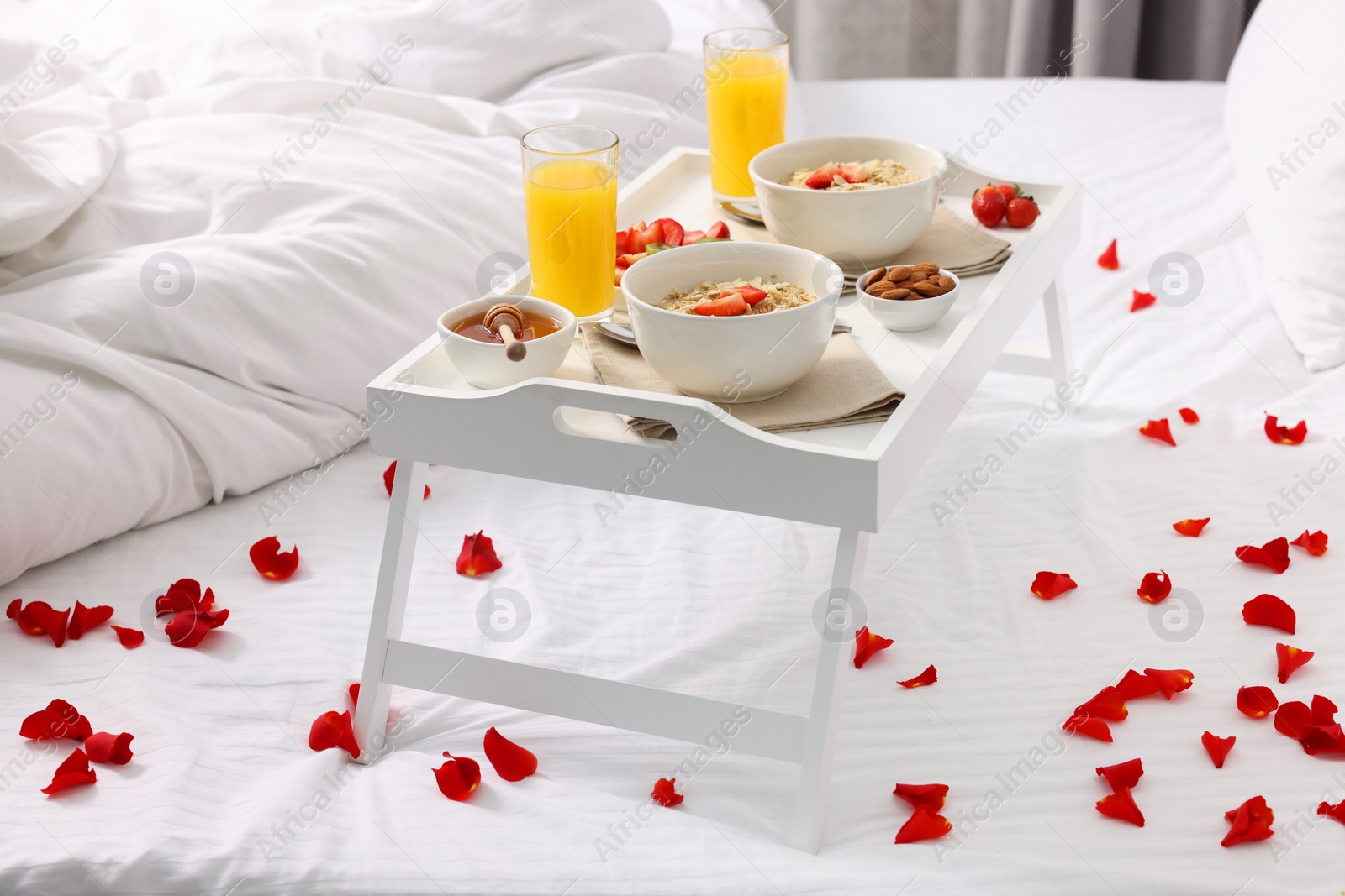 Tray with tasty breakfast and rose petals on bed at home Photo of Tray with tasty breakfast and rose petals on bed at home