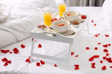 Photo of Tray with tasty breakfast and rose petals on bed at home