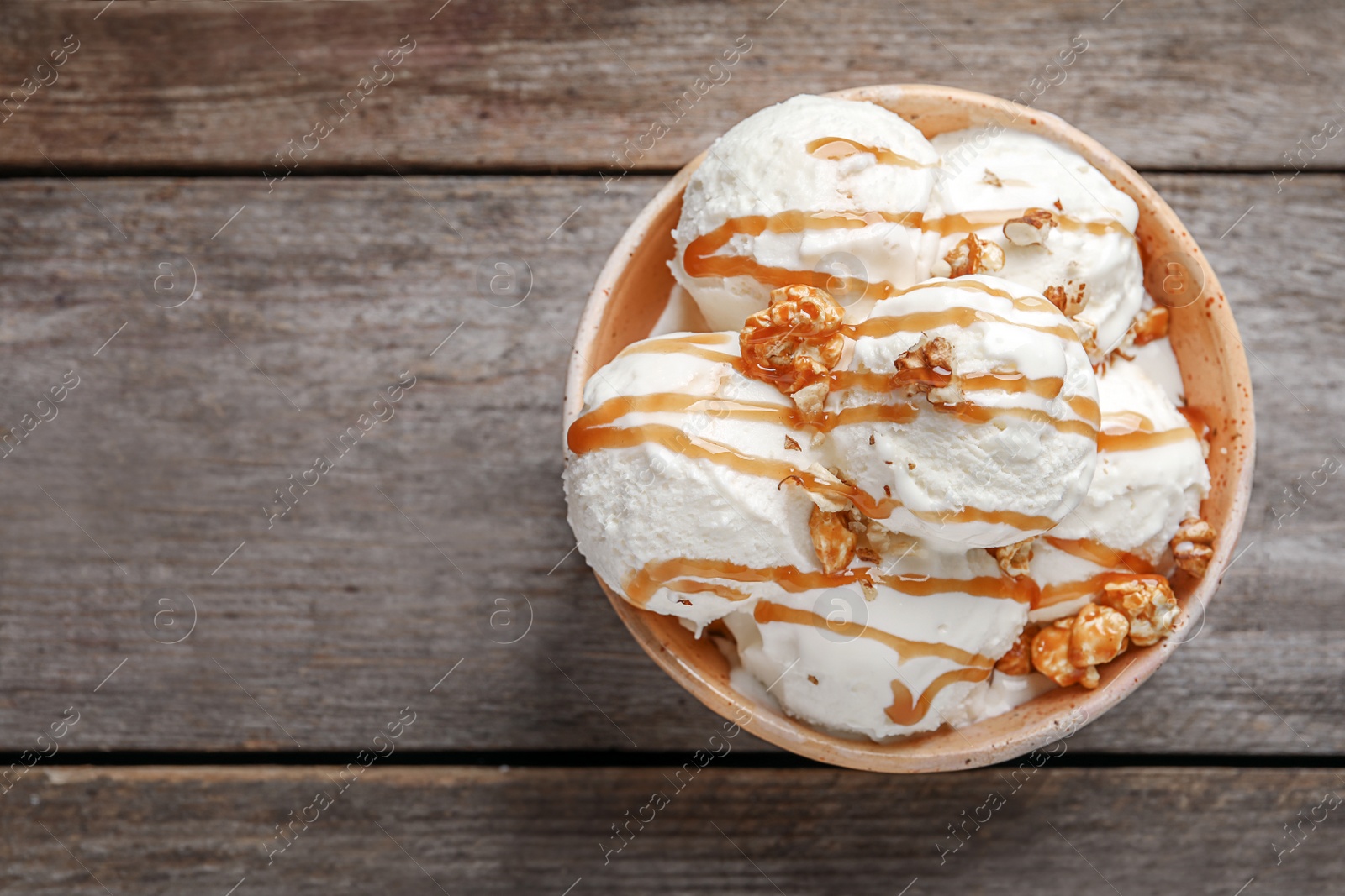 Photo of Tasty ice cream with caramel sauce and popcorn in bowl on wooden table, top view