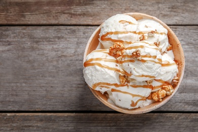 Photo of Tasty ice cream with caramel sauce and popcorn in bowl on wooden table, top view