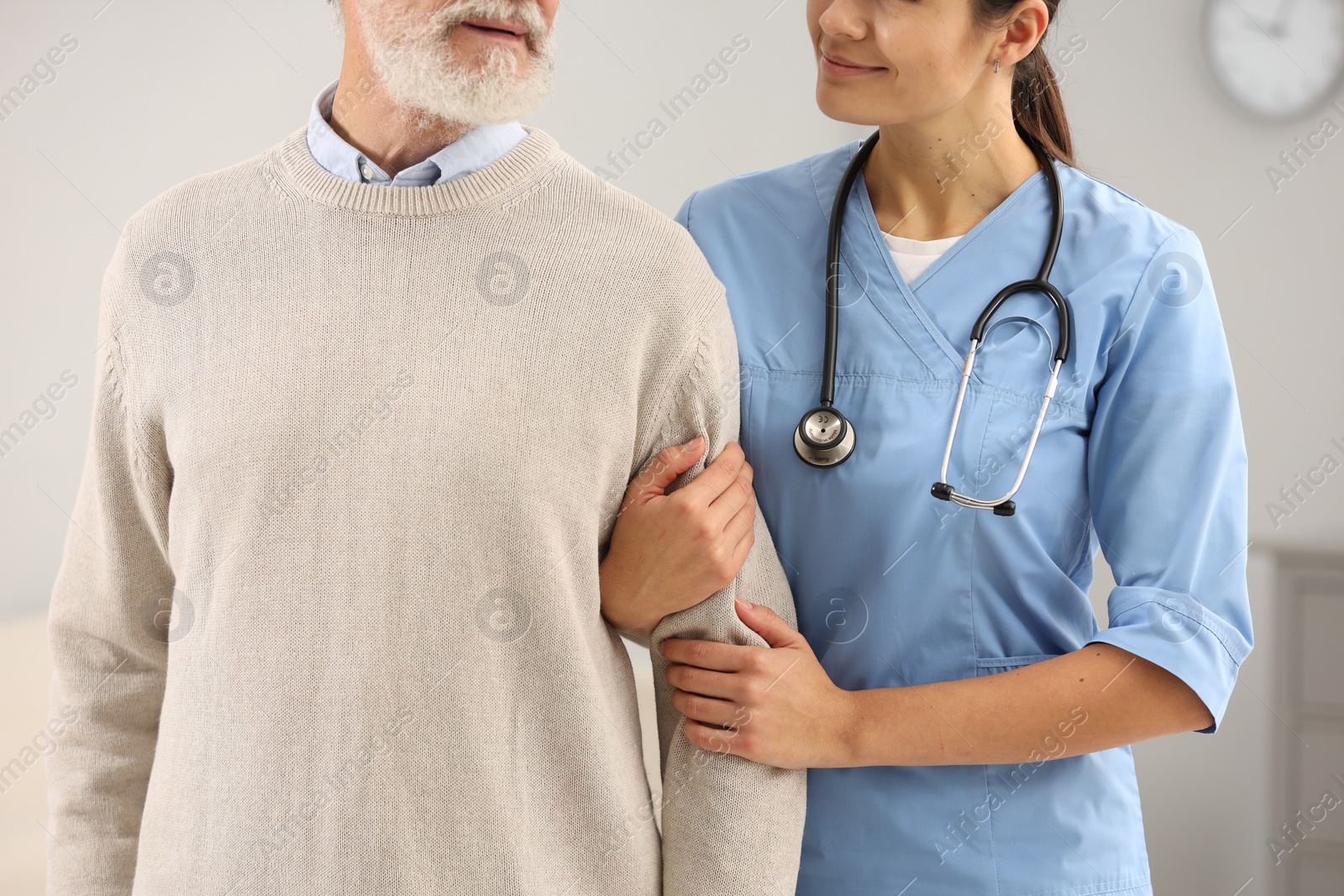 Photo of Nurse supporting elderly patient indoors, closeup view